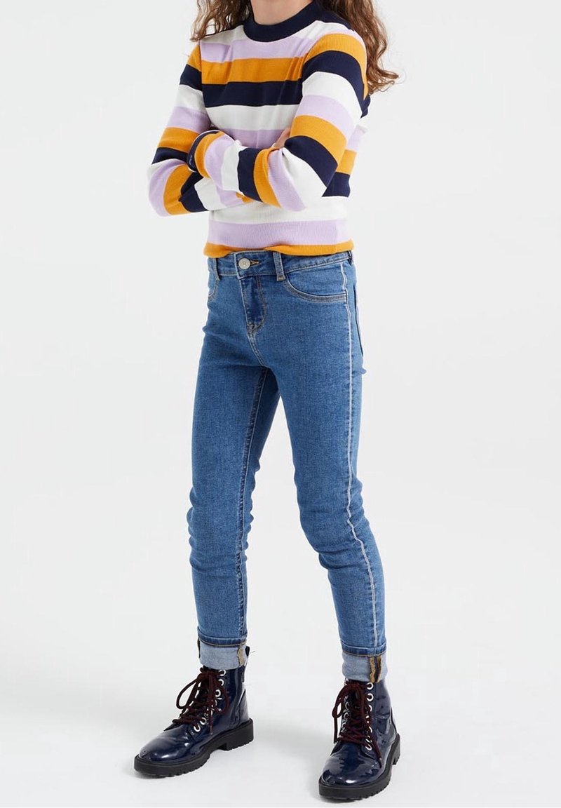 Randig tröja i gult, lila och marinblått, i kombination med blå skinny jeans. Den avslutande touchen är blanka marinblå kängor med snörning.