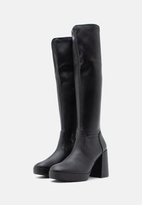 Bottes noires en cuir jusqu'aux genoux avec un talon bloc massif, texture lisse, bout rond et détails de coutures minimaux.