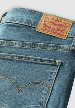 Jasnoniebieskie dżinsy z pomarańczowymi przeszyciami, z brązową skórzaną metką z napisem "LEVI STRAUSS & CO." oraz grafiką koni.