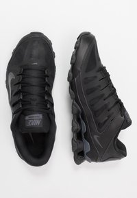 Schwarze Sportschuhe verfügen über ein Obermaterial aus Mesh, eine Schnürung, eine gepolsterte Sohle und strukturierte Akzente. Auffällige Nike-Branding auf der Zunge.