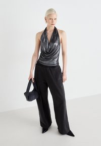 Metallic halterneck-top med draperet halsudskæring, parret med løse sorte brede bukser. Modellen holder en tekstureret sort håndtaske.
