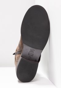 Semelle de botte en cuir marron avec talon et bout en caoutchouc noir, fermeture éclair latérale visible, taille marquée 4½, sur fond blanc et mur d’angle.