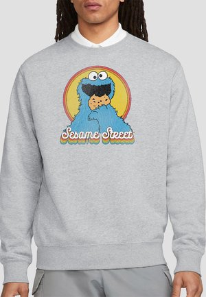 Gray sweatshirt featuring a cartoon character holding a cookie, with "Sesame Street" text in a colorful, retro design. Long sleeves and ribbed cuffs.