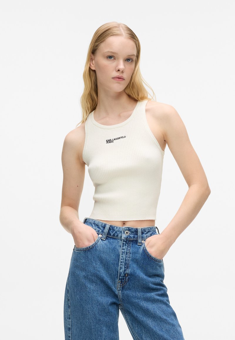 Svetlo béžový rebrovaný crop top s krúhovým výstrihom a čiernym logom "Karl Lagerfeld Jeans". V kombinácii s klasickými modrými džínsami s vysokým pásom.