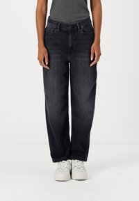 Jeans in denim scuro con una vestibilità rilassata, tasche anteriori e una vita classica, abbinati a sneaker bianche.