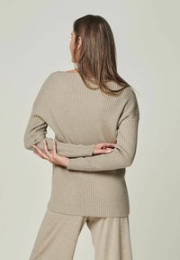 Beige ribbed knit sweater with wide neckline, dropped shoulders, and long sleeves. The texture is soft and stretched, with a relaxed fit.
