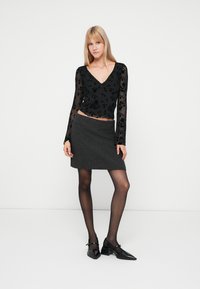 Top preto de renda floral de mangas longas com decote em V, combinado com uma saia mini cinza e sapatos com tira no tornozelo pretos. Textura suave, design ajustado.