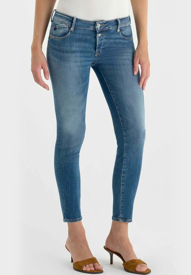 Strakke blauw denim jeans met een vervaagde wassing, vijf zakken, riemlussen en een knoopsluiting. Gekleed met bruine sandalen met hak.