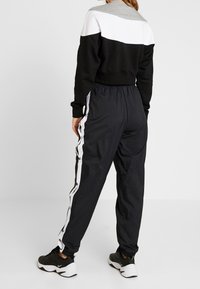 Svart och grå färgblockerad sweatshirt med en kortad design, som parats med svarta träningsbyxor med vita sidostråk och tryckknappar.