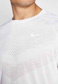 Bijela Nike atletska majica s teksturiranim gradijentnim uzorkom, okruglim izrezom i malim logom na prsima. Glatka tkanina s dizajnom koji prozračuje.