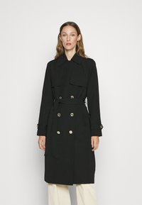 Svart trenchcoat laget av lett stoff, med dobbelspent gullknapper, store revers og et matchende belte i midjen.