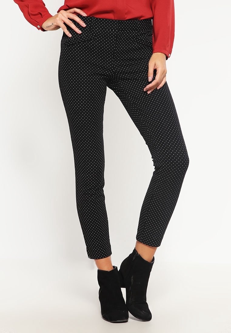Leggings noirs ajustés avec des pois blancs, présentant une texture lisse et une taille mi-haute, associés à des bottes noires à chevilles.
