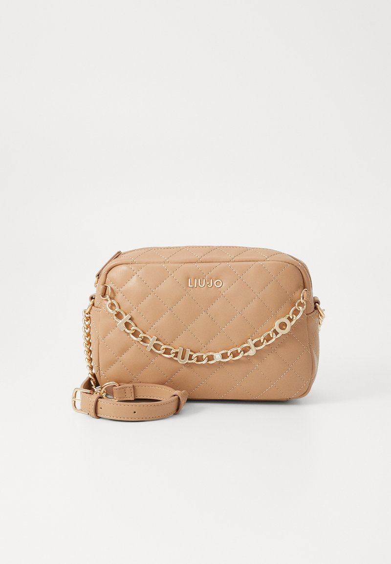 Bolso de mano acolchado en tono beige con un acento de cadena dorada, correa ajustable y cierre con cremallera. Presenta un detalle del logo en la parte frontal. Forma rectangular compacta.