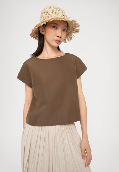 Haut marron à manches courtes avec un col arrondi, associé à une jupe beige plissée. Le mannequin porte un chapeau en paille beige avec des bords frangés.