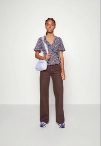 Top envolvente floral preto com mangas curtas com babados, calças largas castanhas e uma mala de ombro azul clara, combinadas com ténis azul e branco.