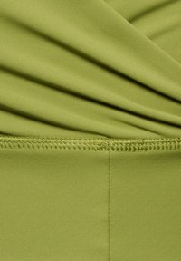 Zielony elastyczny materiał z zebranym teksturą. Charakteryzuje się gładką powierzchnią i widocznymi szwami wzdłuż szwa dla dodatkowego detalu.