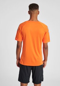Felgekleurde oranje sportshirt met korte mouwen en een textuurpatroon, gecombineerd met zwarte shorts. Heeft raglan mouwen en een ronde hals.