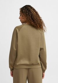 Sudadera color caqui con un corte relajado, puños y dobladillo acanalados. Textura suave; las mangas raglán ofrecen mayor libertad de movimiento y comodidad.