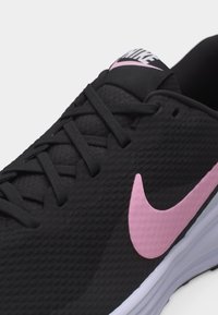 Μαύρο αθλητικό παπούτσι Nike με ροζ λογότυπο Swoosh, μαύρα κορδόνια και λευκή σόλα, που δείχνει κοντινή λήψη των λεπτομερειών στην επάνω πλευρά και τη γλώσσα.