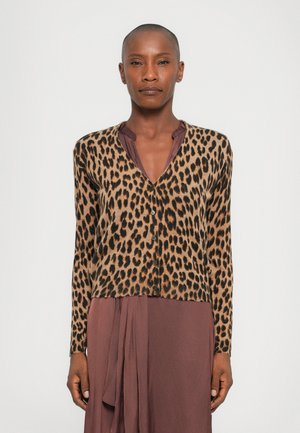 Cardigan con stampa leopardata e maniche lunghe, progettato in tonalità di marrone e beige, con bottoni neri e orlo corto. Indossato sopra un vestito di un profondo color malva.