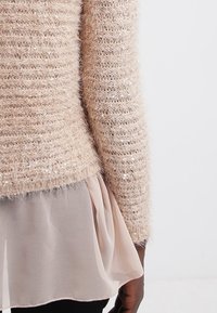 Mjuk beige stickad tröja med en texturerad, fluffig yta, med subtila paljetter och ett lager av ljusbeige chiffong under.