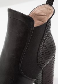 Bottine noire en cuir lisse et tissu texturé, avec un côté à motifs et un talon noir uni.