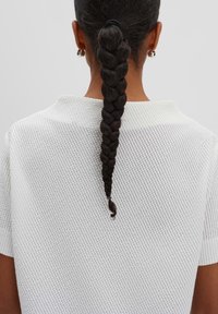 White, textured knit top with a round neckline, seen from the back, featuring a braided ponytail secured with a band.