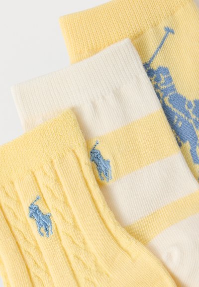 Τρεις διπλωμένες κάλτσες σε απαλό κίτρινο και λευκό, με μπλε κεντημένα λογότυπα παικτών πόλο και ριγέ και υφασμένες υφές.