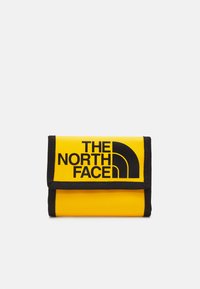 Żółty portfel z czarnym logo The North Face. Wykonany z wytrzymałego materiału, posiada klapkę złożoną na dół i czarne wykończenia. Kompaktowy prostokątny kształt.