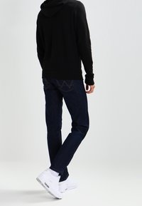 Felpa nera con un design aderente, abbinata a jeans blu scuri. Sneakers bianche con accenti visibili e ammortizzazione.