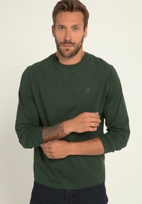 Langärmliges grünes T-Shirt aus weichem Stoff. Mit rundem Halsauschnitt und dezentem "JP"-Logo oben links. Glatte, ungemusterte Textur.