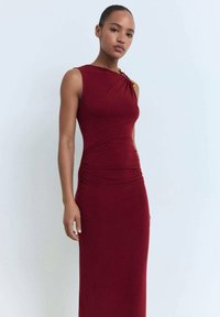Robe sans manches de couleur bordeaux avec un côté froncé et un matériel décoratif à l'épaule. Tissu lisse et extensible avec une silhouette ajustée.