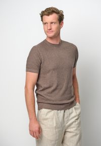 Brązowy krótki sweter dzianinowy z okrągłym dekoltem, w połączeniu z jasnymi spodniami lnianymi, które mają teksturowane wykończenie.