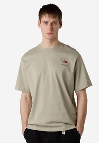 Lichtbeige katoenen t-shirt met korte mouwen, ronde hals, klein rood vierkant logo op de linkerborst, losse pasvorm, minimalistisch ontwerp.