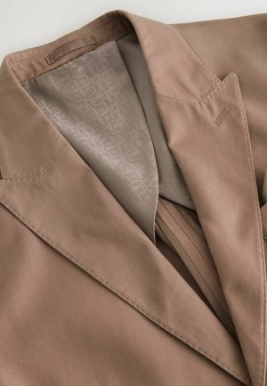 Brauner Blazer mit strukturierten Schultern, Revers und subtilen Stickdetails. Das Innere hat eine gemusterte Fütterung in einem hellbeigen Farbton.