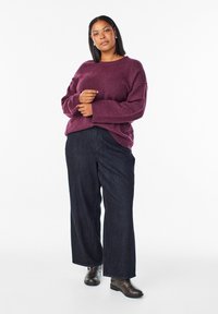 Burgundska pletena majica s širokim rukavima, uparena s tamnoplavim širokim trapericama i smeškim čizmama do gležnjeva. Jednostavni, teksturirani materijali.