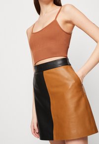 Un crop top côtelé marron associé à une jupe en cuir, avec un bloc de couleurs noir et marron, des poches latérales et une silhouette ajustée.