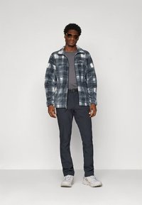 Fliso striukė su juodai balta languota rašte, užsegama užtrauktuku, derinama su pilka marškinėliais ir tamsiomis kelnėmis, dėvima su saulės akiniais ir sportbačiais.