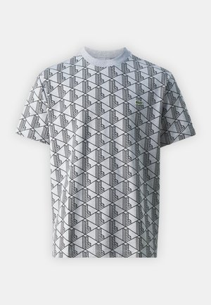 T-shirt gris à manches courtes avec un motif géométrique noir. Comprend un petit logo vert brodé sur la poitrine. Matière en coton.