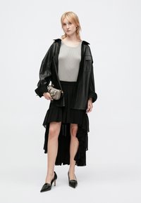 Veste en cuir noir surdimensionnée, haut rayé gris, jupe noire à volants et à niveaux, et escarpins noirs à bout pointu. Sac à main avec des accents dorés.