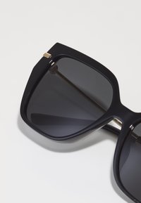 Ochelari de soare supradimensionați negri cu lentile întunecate, rame rectangulare plate și accesorii aurii la tâmple. Finisaj neted și lucios.