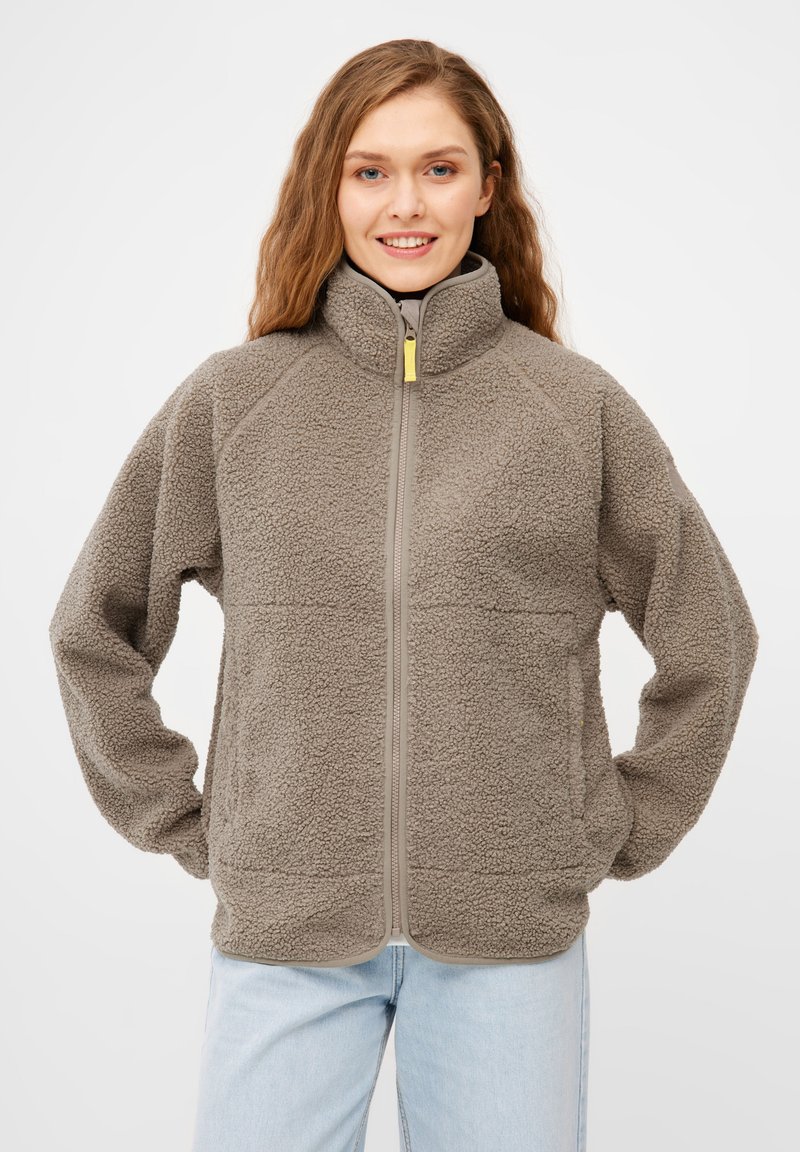 Flauschige beiger Fleecejacke mit hohem Kragen, frontalem Reißverschluss und grauen Akzenten. Verfügt über Seitentaschen und eine strukturierte Oberfläche.