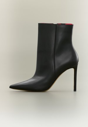 Stivaletto in pelle nera con punta affilata e tacco a stiletto alto su sfondo neutro.