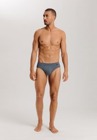 Grijze slips gemaakt van zachte stof, met een effen kleur en een comfortabele tailleband. Het model heeft een gespierd postuur en staat blootvoets.