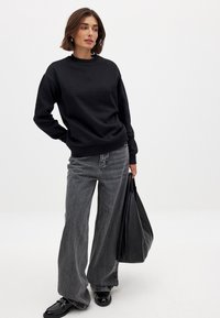 Zwarte sweatshirt met een ronde hals, gecombineerd met lichtgrijze wijde jeans en een zwarte schoudertas. Soepele texturen, ontspannen pasvorm.
