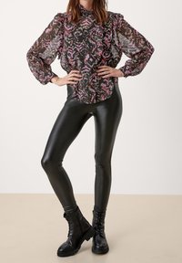 Black and pink patterned lightweight blouse with ruffles, paired with shiny black leggings and black lace-up boots. Smooth texture and fitted design.