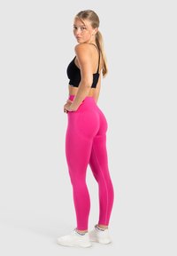 Vaaleanpunaiset legginssit joustavasta kankaasta, korkea vyötärö ja koristella saumoilla, yhdistetty mustaan lyhythihaiseen toppiin ja valkoisiin tennareihin.