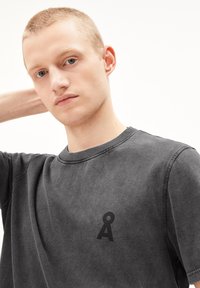 Zwarte katoenen t-shirt met korte mouwen, kenmerken van een geribbelde ronde halslijn en een klein zwart logo op de borst, met een vervaagde, gestructureerde afwerking.