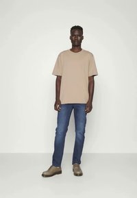 Beige crew-neck t-shirt, blue denim jeans, and gray casual shoes. Simple design, relaxed fit, and smooth texture throughout.