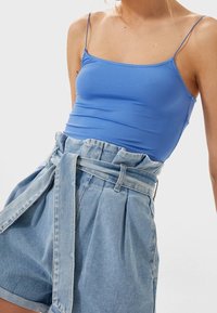 Blauw aansluitend tanktop met dunne bandjes, gecombineerd met high-waisted denim shorts met een strikceintuur en geplooid ontwerp in een lichte wassing.